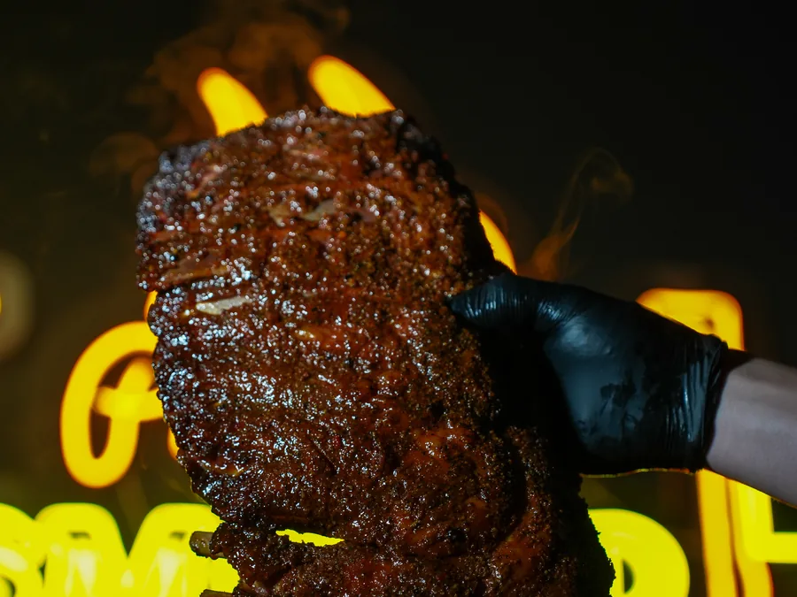 A slab of slow-smoked Angus beef cheek held up against the neon sign