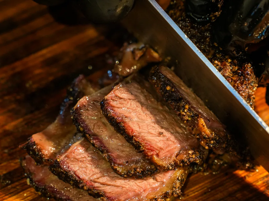 Black Angus short rib being sliced thick across the bone on a wooden board